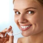 Woman smiling while inserting an Invisalign clear aligner tray.