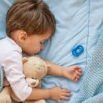 Toddler sleeping peacefully with teddy bear, illustrating child sleep quality related to orthodontic treatment.
