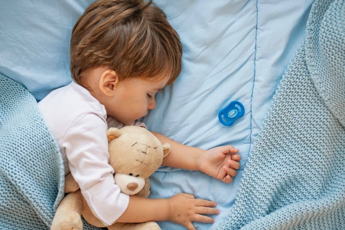 Toddler sleeping peacefully with teddy bear, illustrating child sleep quality related to orthodontic treatment.