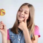 Girl with braces holding colorful lollipop, considering chewy candy effects on orthodontic treatment.