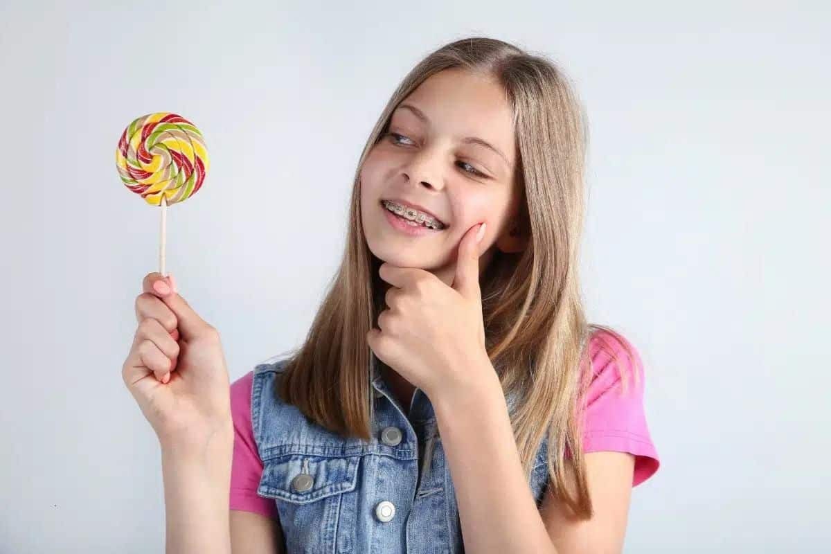 Girl with braces holding colorful lollipop, considering chewy candy effects on orthodontic treatment.