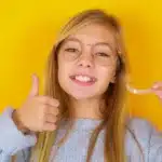 Smiling teenage girl with glasses giving thumbs up, representing positive orthodontic treatment results.