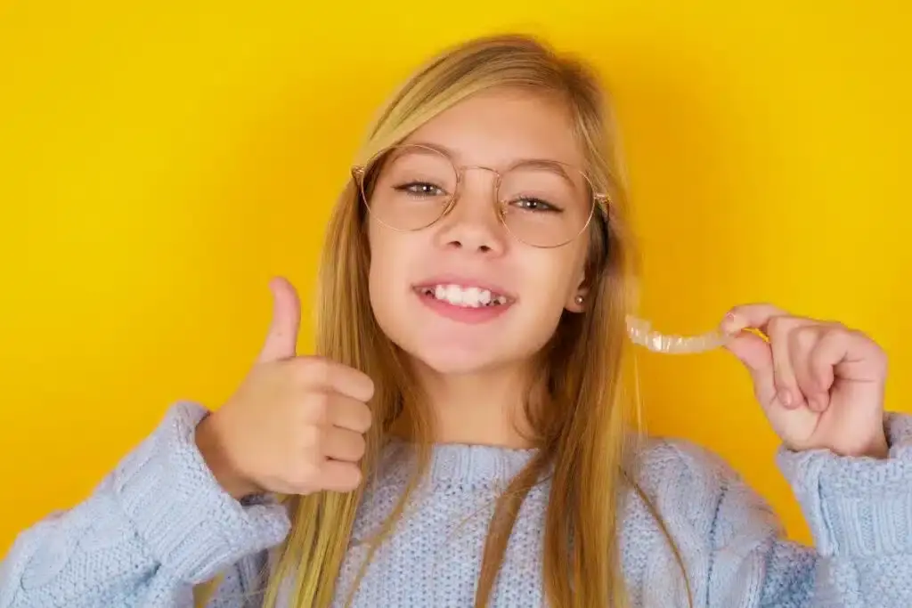 Smiling teenage girl with glasses giving thumbs up, representing positive orthodontic treatment results.