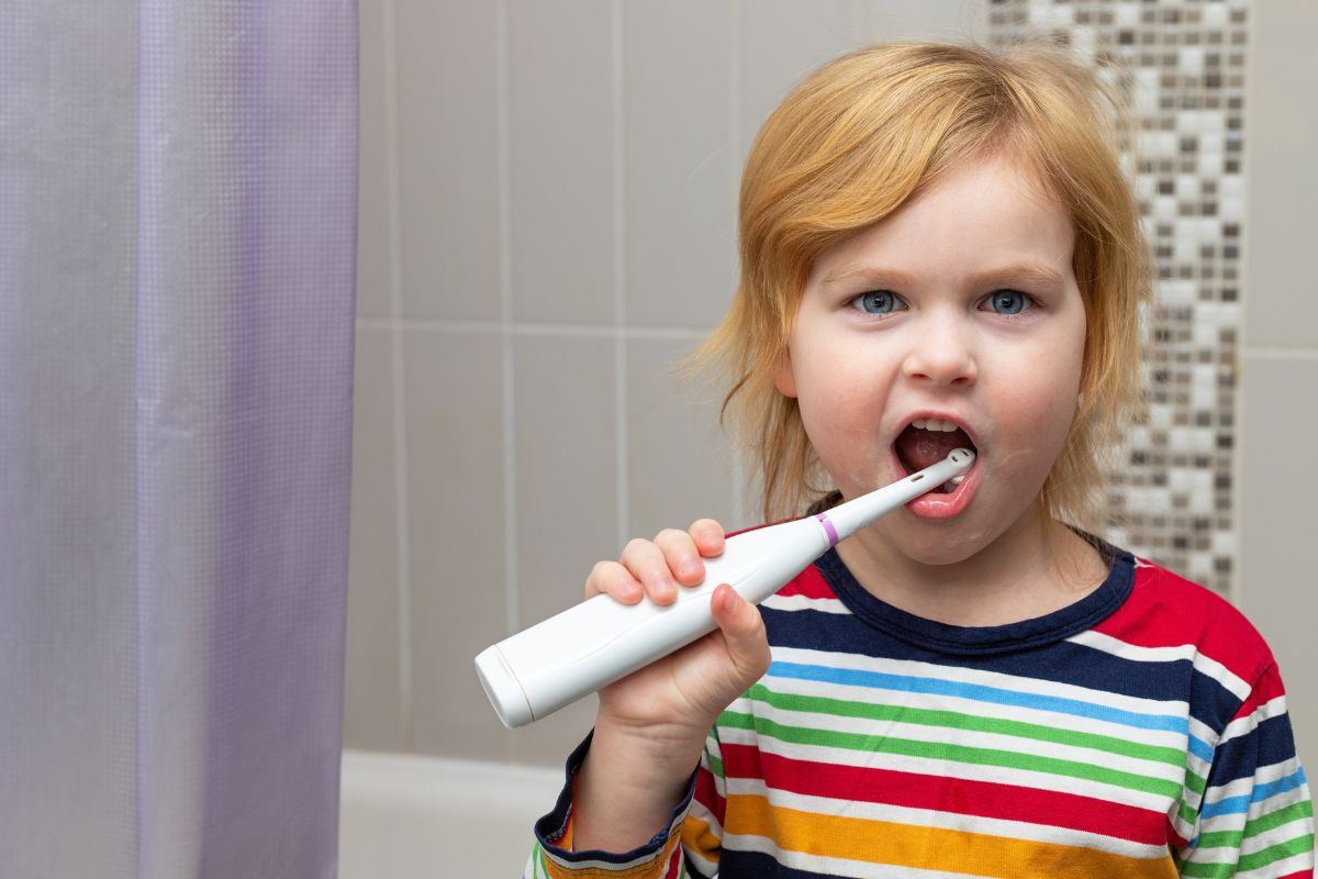 Young child brushing teeth with electric toothbrush in bathroom.