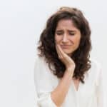 Woman experiencing tooth pain, holding her cheek in discomfort from an impacted tooth.
