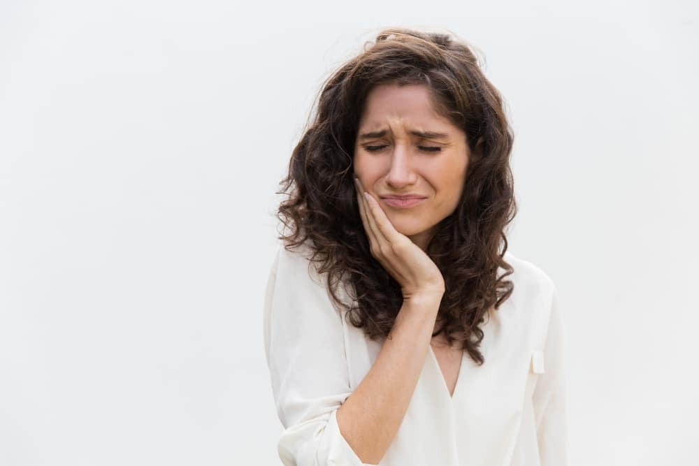Woman experiencing tooth pain, holding her cheek in discomfort from an impacted tooth.