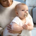 Mother holding infant with pacifier, demonstrating teething comfort for babies in Spring, TX.