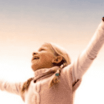 Happy child with arms raised celebrating a bright smile outdoors.