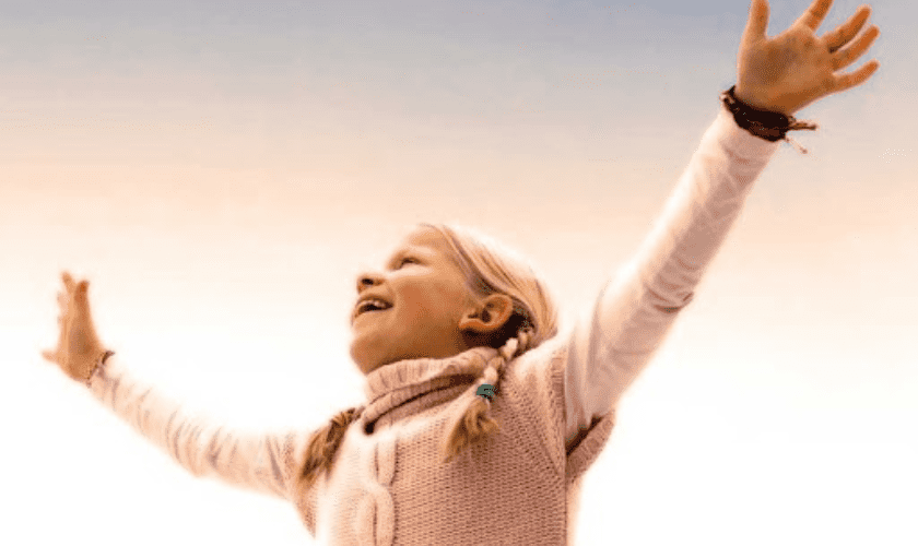 Happy child with arms raised celebrating a bright smile outdoors.