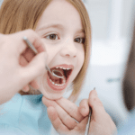 Young child receiving dental examination with mouth open during checkup at dentist office.