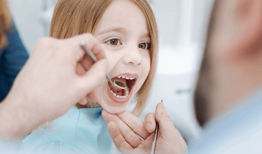 Young child receiving dental examination with mouth open during checkup at dentist office.