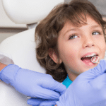 Young child receiving dental examination in treatment chair with dentist wearing blue gloves.