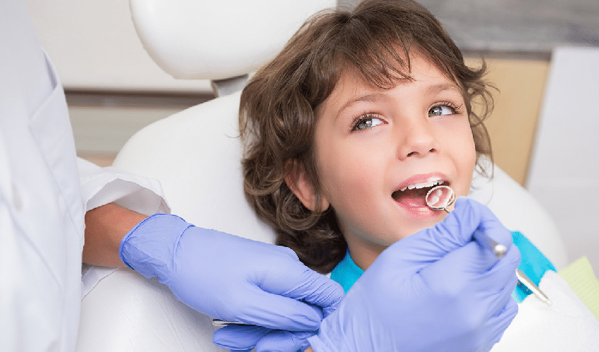 Young child receiving dental examination in treatment chair with dentist wearing blue gloves.