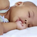 Sleeping newborn infant with hand near mouth, illustrating thumb sucking habits in babies.