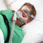 Child wearing CPAP mask during sleep apnea treatment in bed.