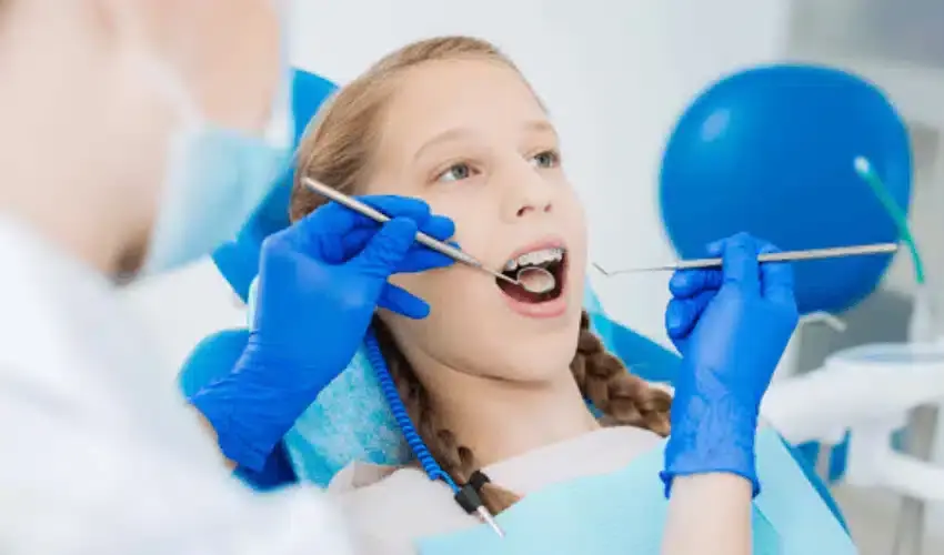 Young girl receiving pediatric dental examination with dentist using tools and mirror.