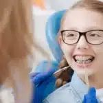 Young patient with braces and glasses smiling during dental examination in Spring, TX.