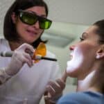 Dentist applying laser treatment to patient's face during TMJ disorder management procedure.