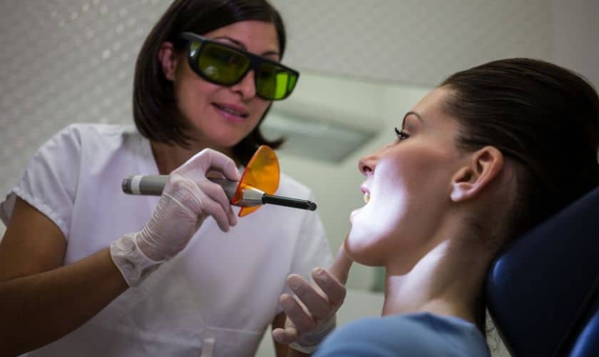 Dentist applying laser treatment to patient's face during TMJ disorder management procedure.