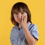 Child with hand to cheek showing signs of TMJ pain or discomfort.