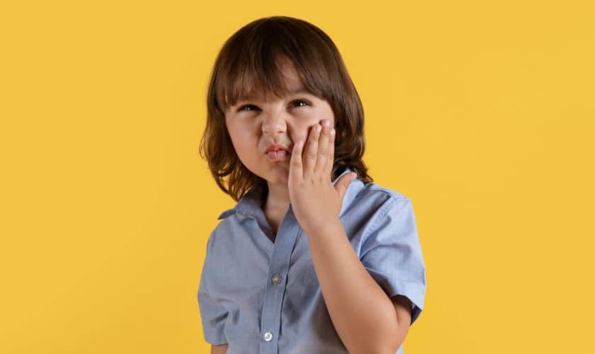 Child with hand to cheek showing signs of TMJ pain or discomfort.