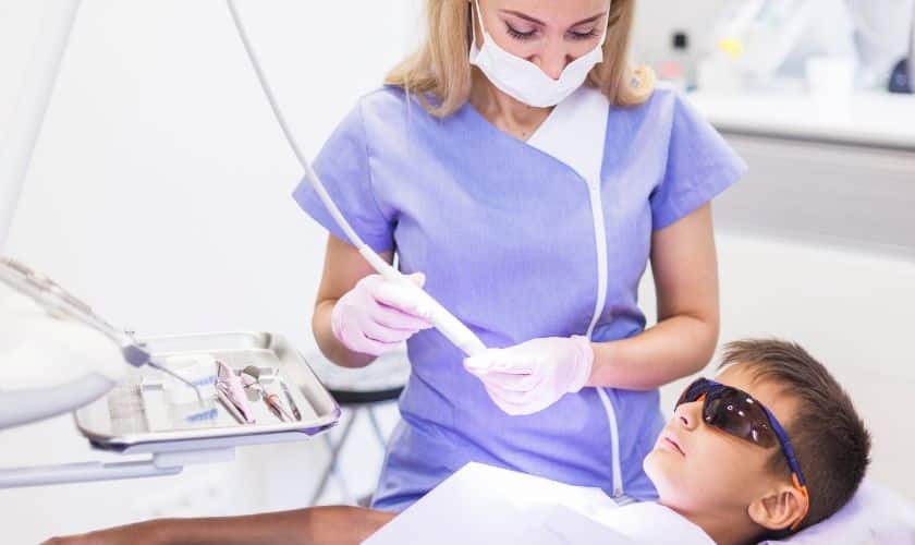 Young child wearing protective eyewear receiving pediatric dental treatment from hygienist in Spring, TX.