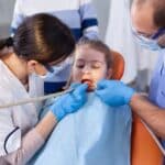 Pediatric dental exam with female dentist and male assistant treating young girl in Spring, TX.