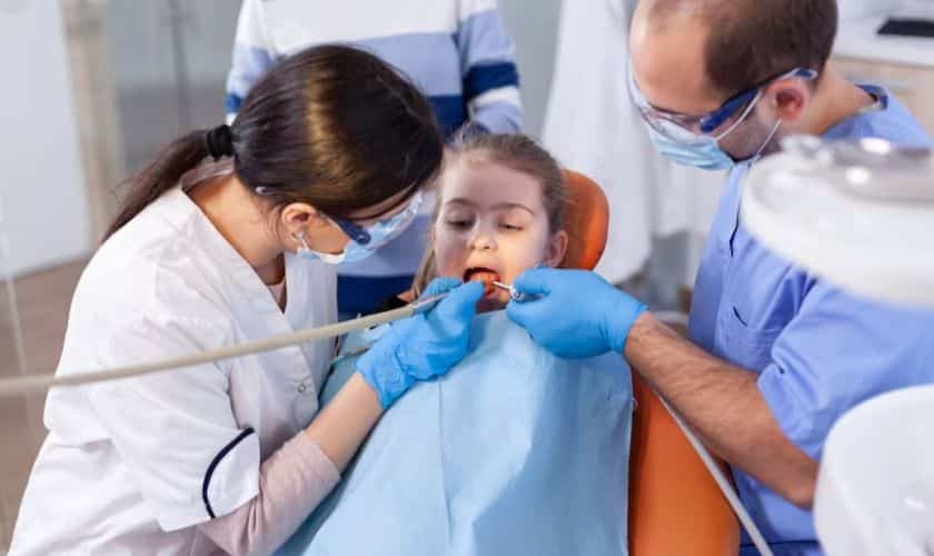Pediatric dental exam with female dentist and male assistant treating young girl in Spring, TX.