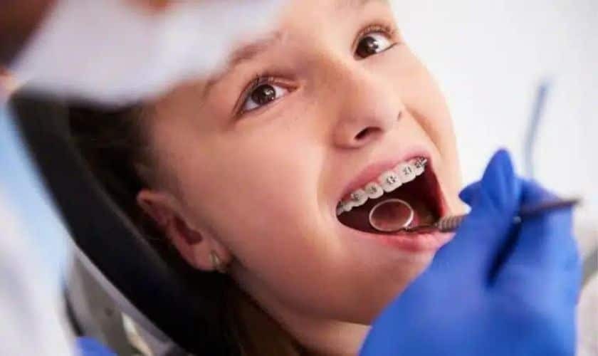 Young patient with metal braces receiving dental examination from orthodontist in blue gloves.