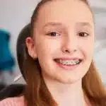 Teen patient with metal braces smiling in modern dental office setting.