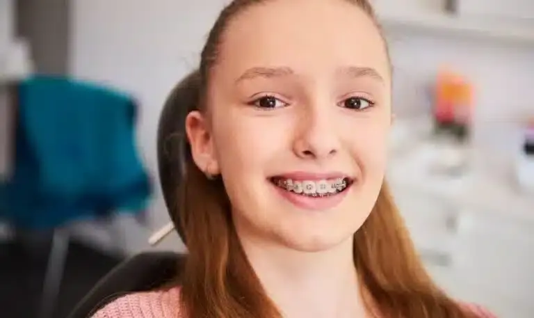 Teen patient with metal braces smiling in modern dental office setting.
