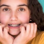Young patient displaying metal braces and confident smile against turquoise background.