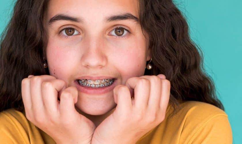 Young patient displaying metal braces and confident smile against turquoise background.