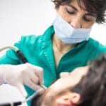 Orthodontist in green scrubs and mask examining young patient during dental treatment.