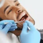 Dentist examining patient's teeth during dental checkup with dental tools.