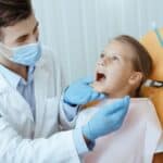 Pediatric dentist examining a young girl's mouth in the dental chair at Spring, TX practice.
