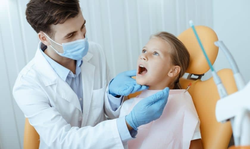 Pediatric dentist examining a young girl's mouth in the dental chair at Spring, TX practice.