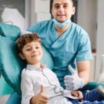 Young boy giving thumbs up with pediatric dentist in treatment room in Spring, TX.