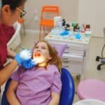 Pediatric dentist examining young patient's teeth in dental chair during routine checkup.