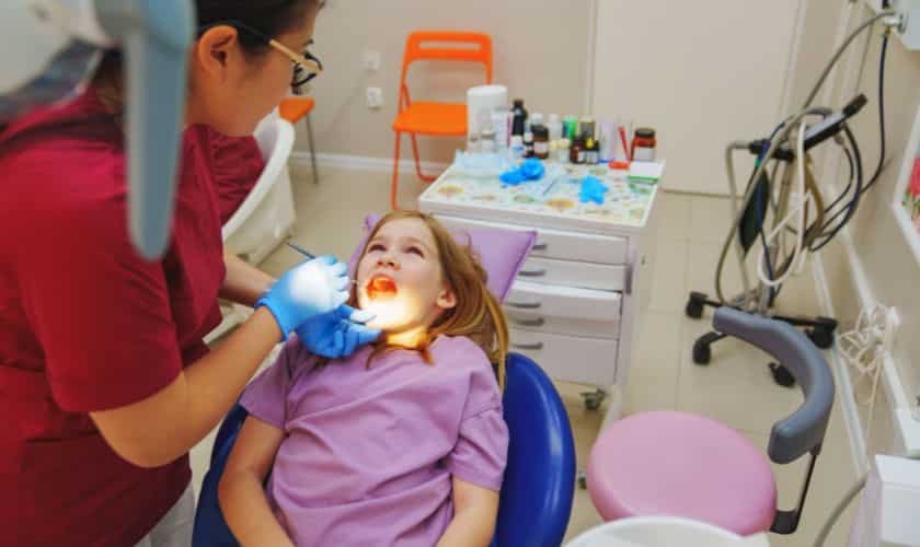 Pediatric dentist examining young patient's teeth in dental chair during routine checkup.