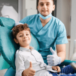 Pediatric dentist with young patient giving thumbs up in dental office treatment room.