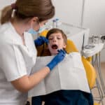 Pediatric dentist examining young boy's teeth in dental chair during routine checkup.