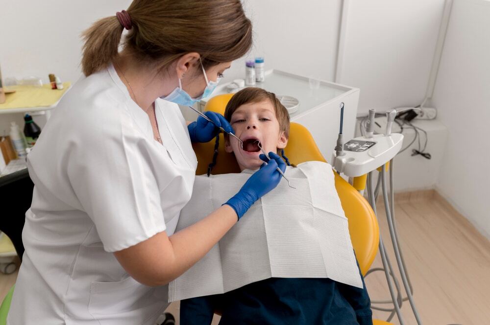 Pediatric dentist examining young boy's teeth in dental chair during routine checkup.