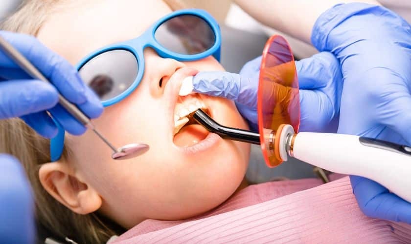 Child receiving laser dental treatment with protective eyewear during pediatric dental procedure.