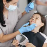 Pediatric dentist examining child's teeth during periodontal therapy consultation.