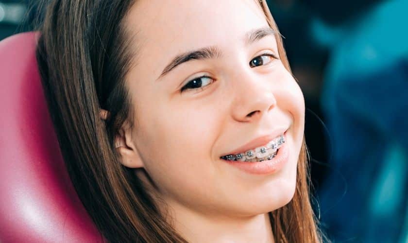 Young patient with dental braces smiling in orthodontic chair during treatment.