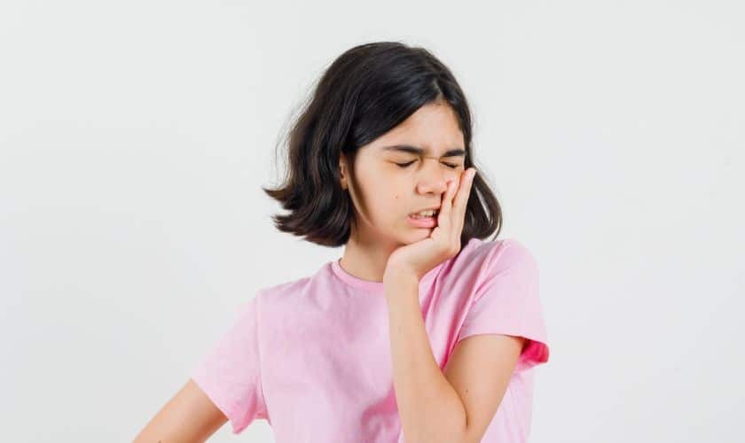 Young girl with hand to cheek showing signs of TMJ pain or discomfort.