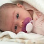 Newborn baby with pacifier demonstrating thumb sucking and pacifier habits discussed in pediatric dental care.