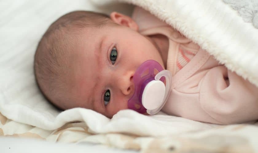 Newborn baby with pacifier demonstrating thumb sucking and pacifier habits discussed in pediatric dental care.