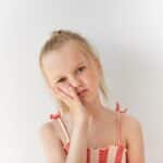 Young girl with hand to cheek showing signs of jaw discomfort or TMJ pain.